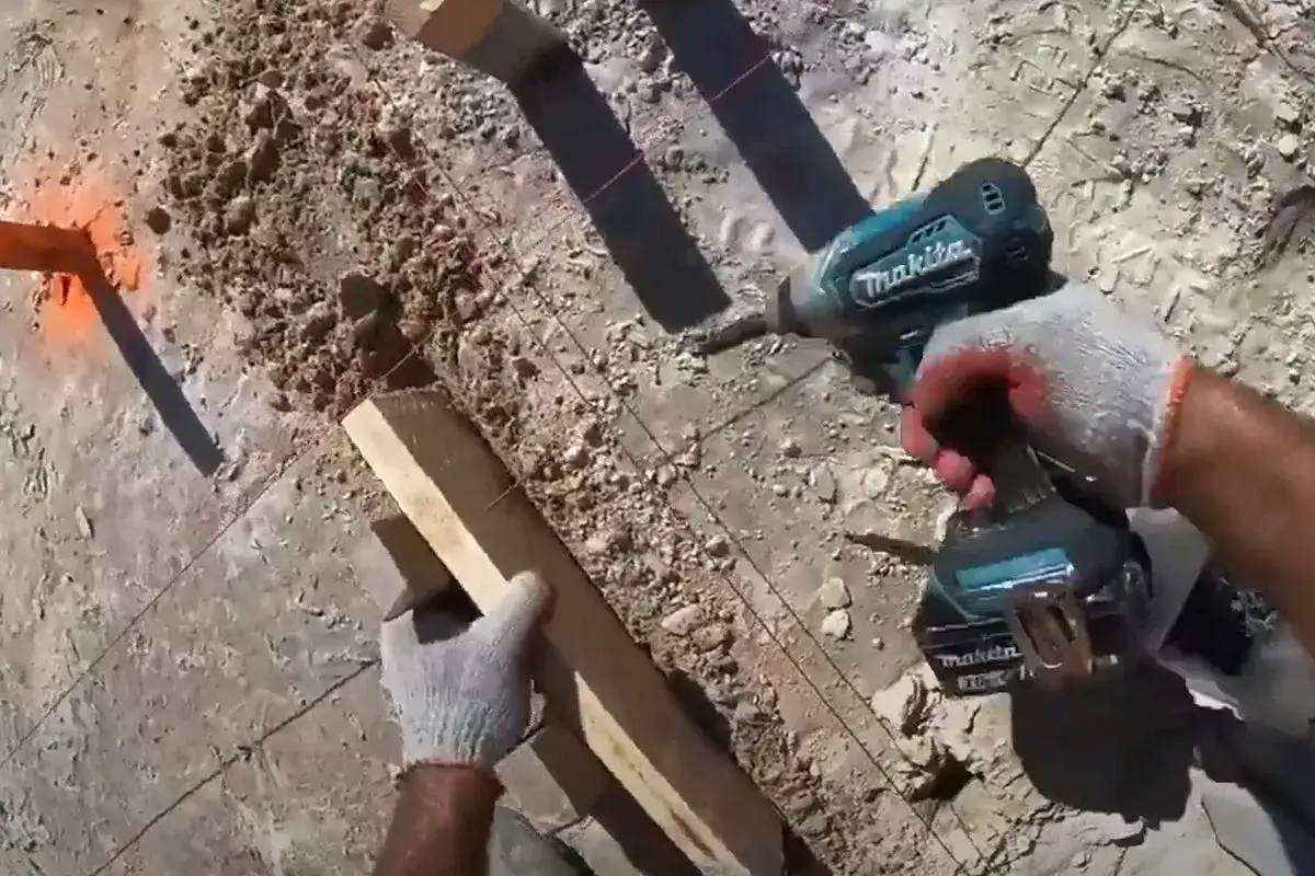 Budowa szalunku pod wylewkę: ręka w rękawicy trzyma drewnianą deskę, obok wiertarko-wkrętarka Makita.