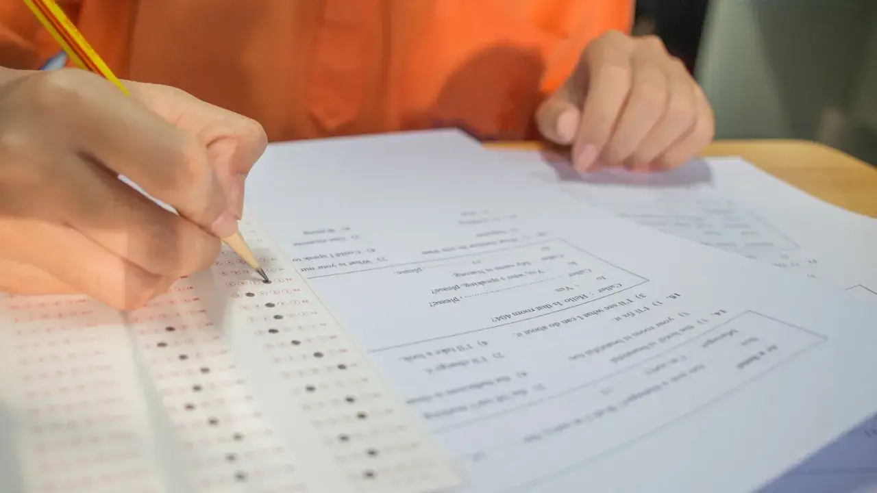 Dłoń z ołówkiem zaznacza odpowiedzi na arkuszu egzaminacyjnym.