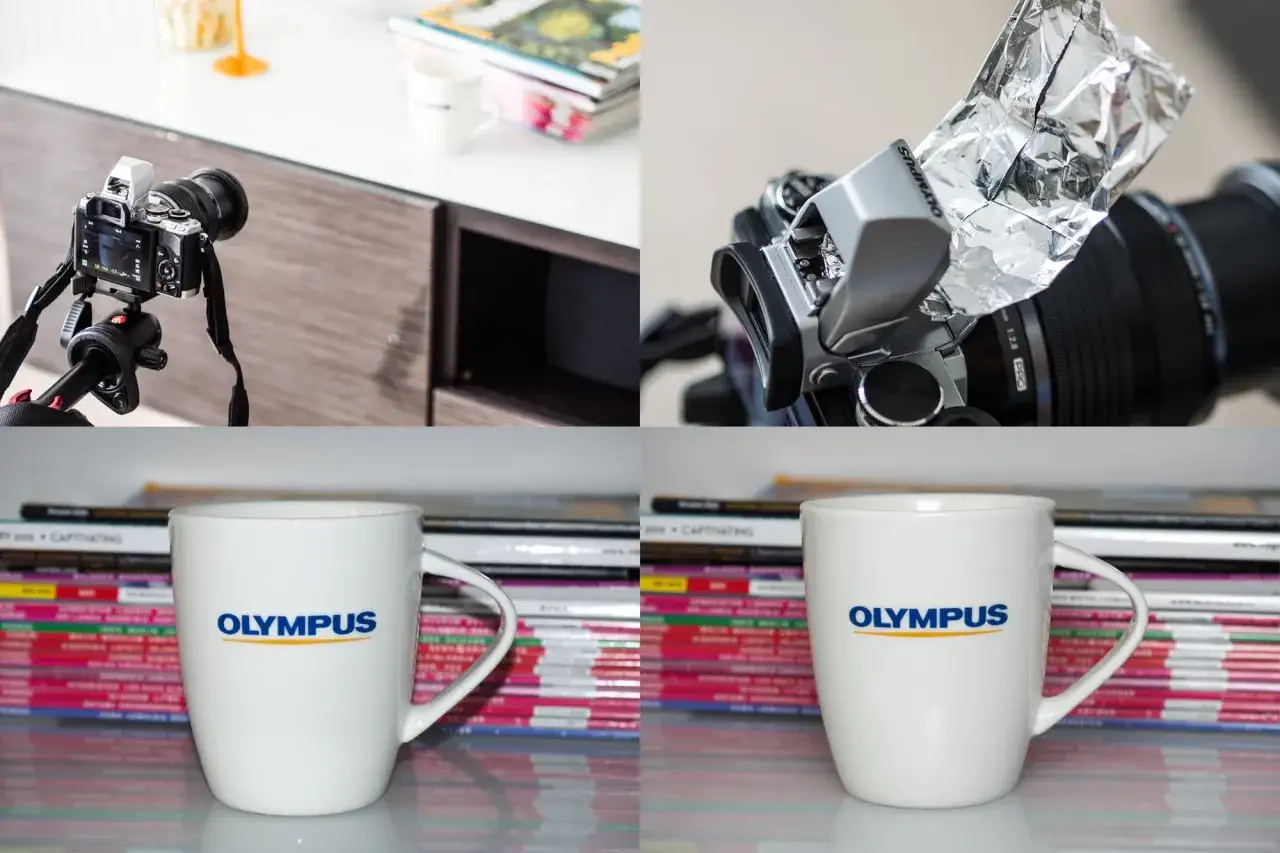 Aparat Olympus z lampą błyskową i dyfuzorem z folii aluminiowej, kubek Olympus na tle stosu magazynów.