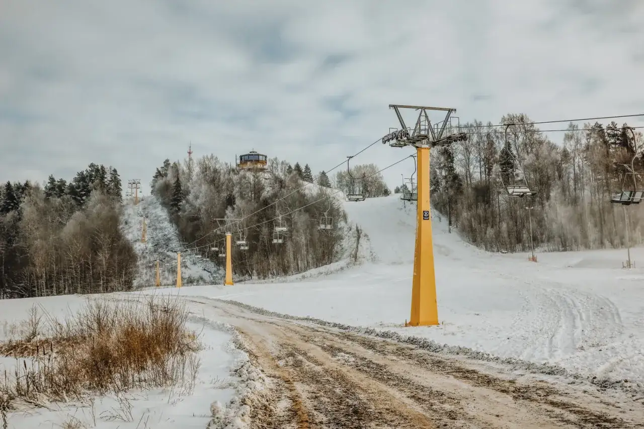 Wyciąg krzesełkowy na ośnieżonym stoku narciarskim z widocznym budynkiem na wzgórzu.