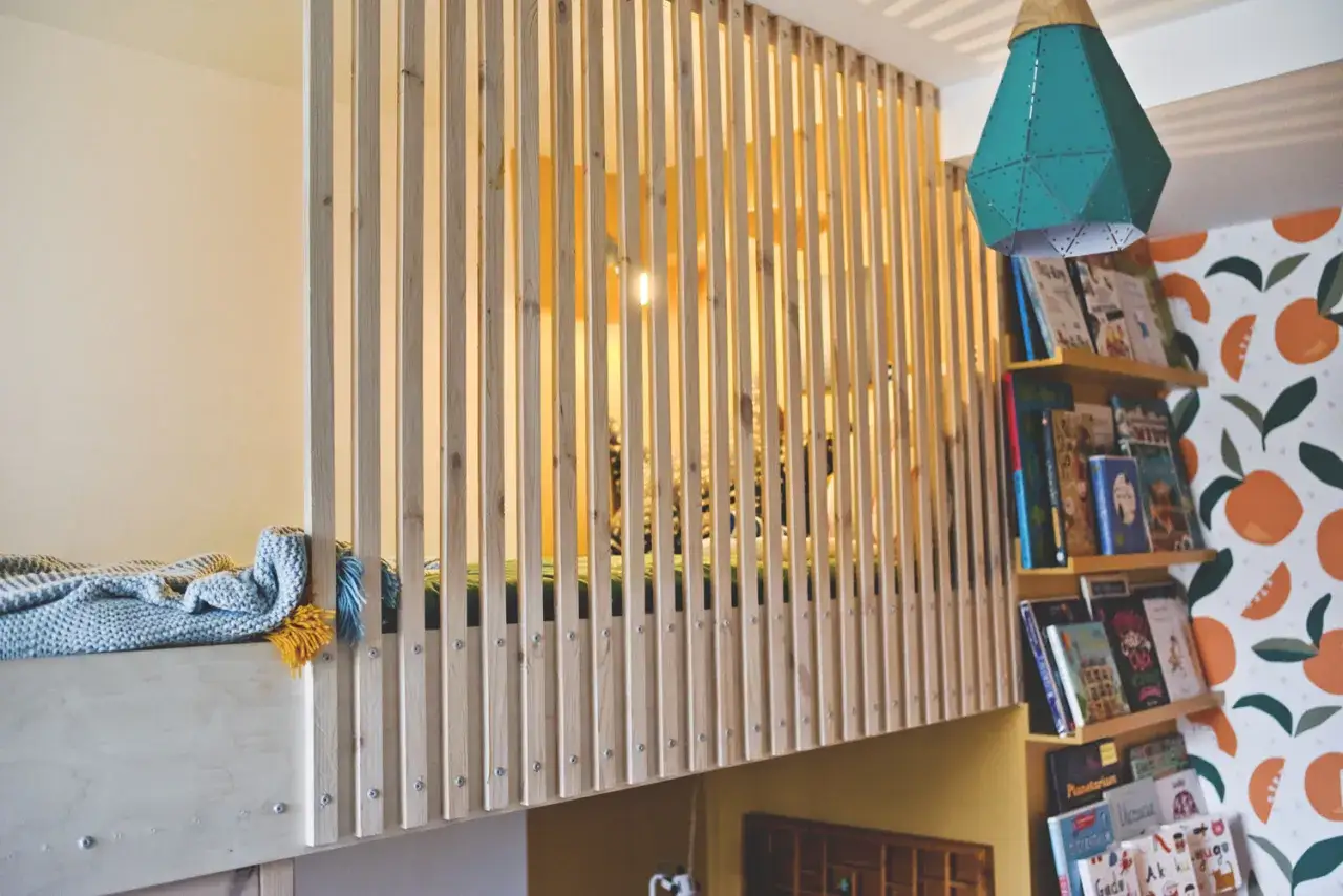 Drewniana antresola z łóżkiem, regał z książkami i kolorowa tapeta z pomarańczami.