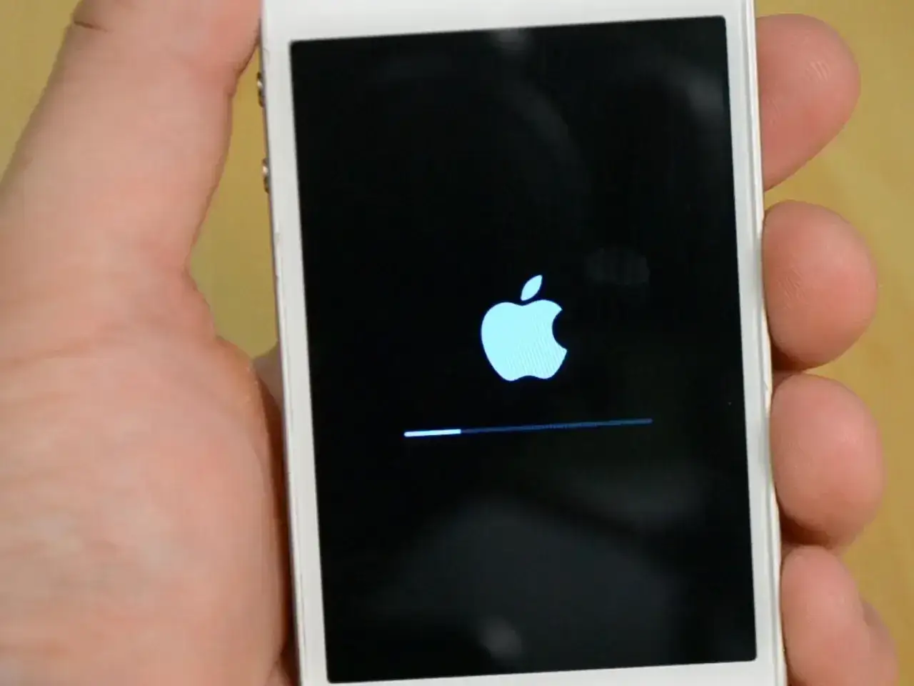 Dłoń trzyma iPhone'a z logo Apple i paskiem postępu, wskazującym na proces hard reset iPhone.