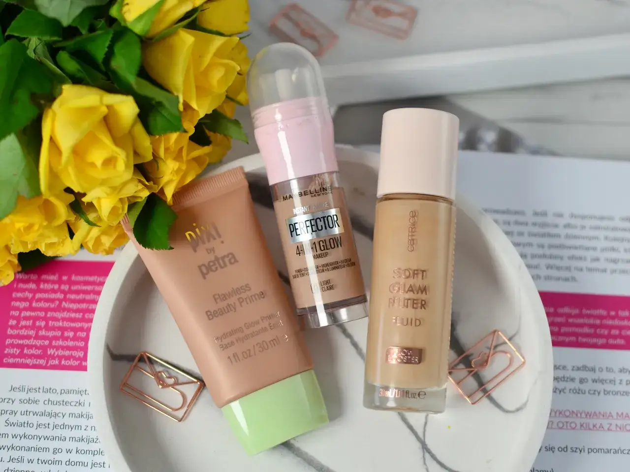 Bazy pod makijaż Pixi, Maybelline i Catrice na tle żółtych róż i ozdobnych spinaczy.