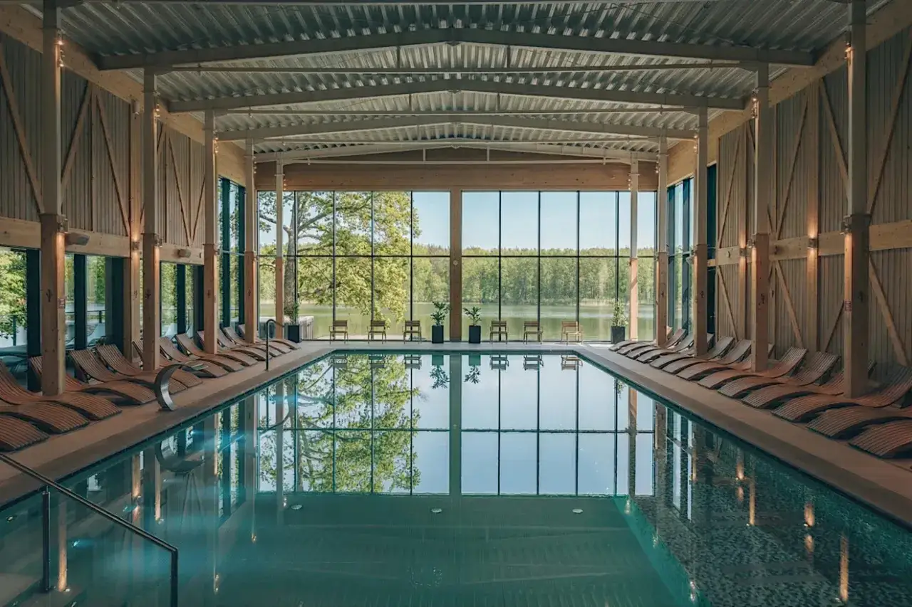 Basen w nowoczesnym spa z widokiem na jezioro i las. Drewniane leżaki i przeszklone ściany tworzą relaksującą atmosferę, idealną dla najlepszego spa w Polsce.