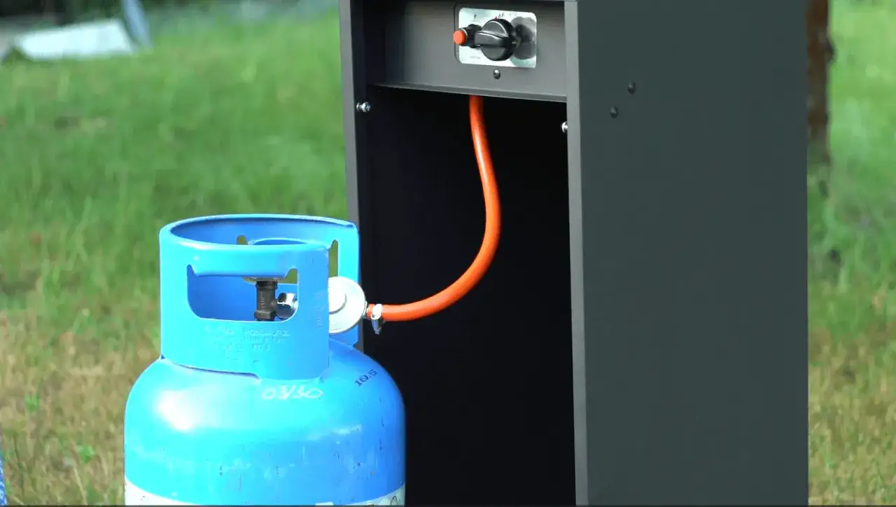 Niebieska butla z gazem LPG podłączona pomarańczowym wężem do czarnej obudowy.
