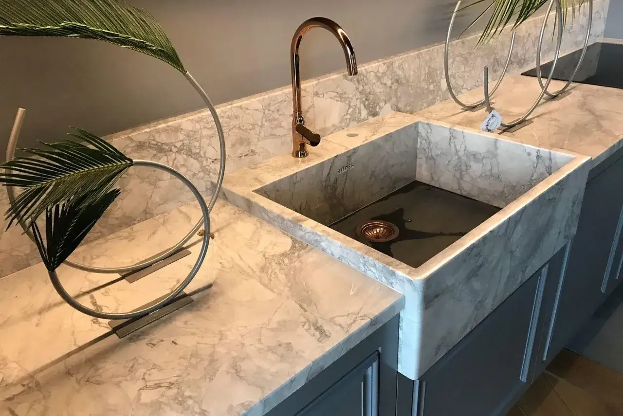 Elegancki zlewozmywak granitowy lub konglomerat w marmurkowym wykończeniu, z miedzianą baterią i ozdobnymi roślinami.