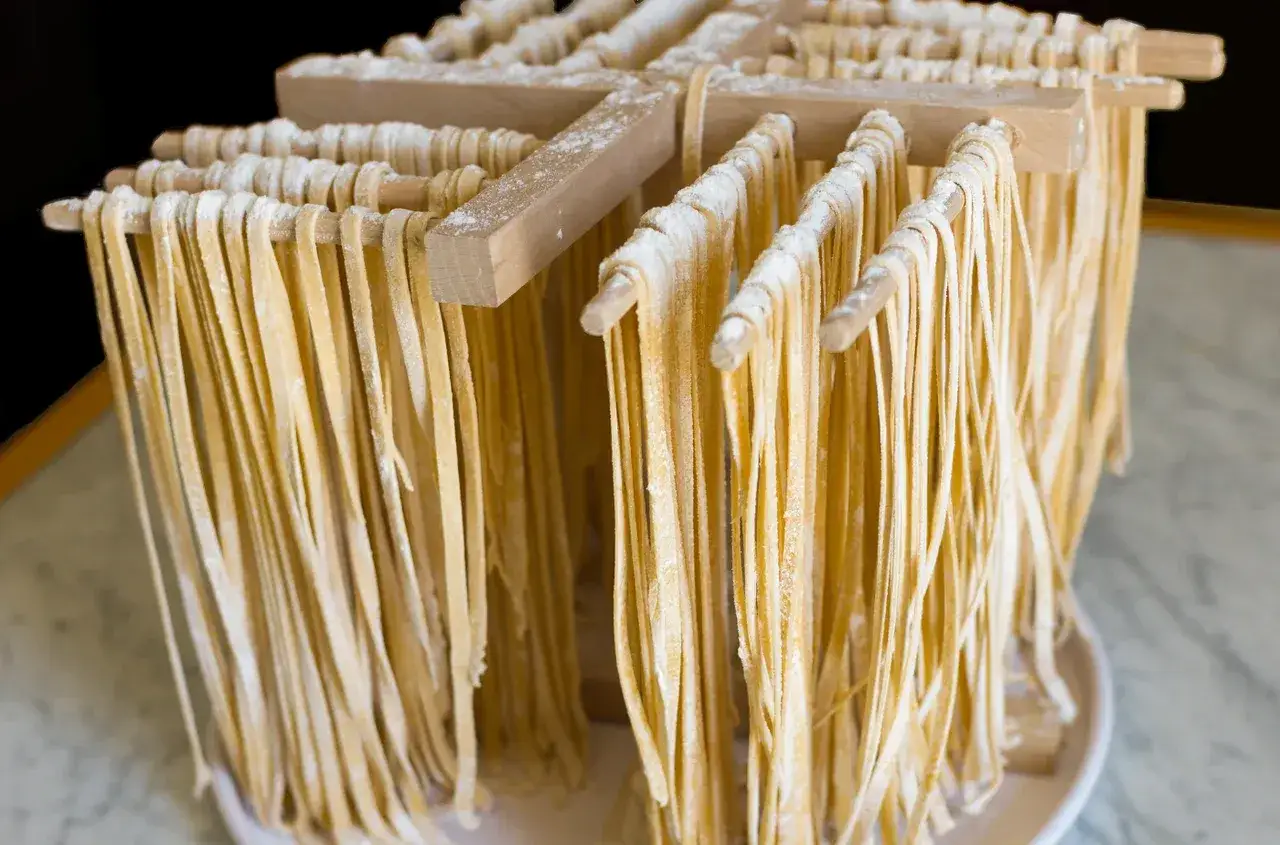 Świeży, domowy makaron w tagliatelle wiszący na drewnianym stojaku do suszenia.