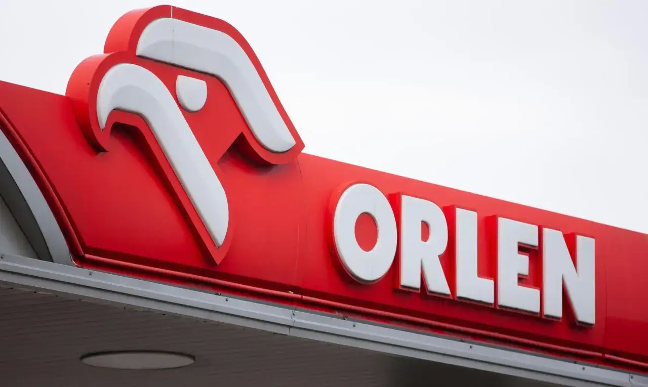 Logo Orlenu na czerwonym tle. Czekamy na moment, kiedy Orlen wypłaca dywidendę, a akcjonariusze cieszą się zyskami.