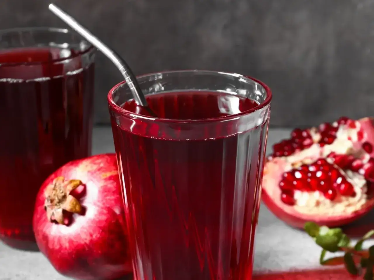 Szklanka z sokiem z granatów, obok owoców. Czy sok malinowy obniża ciśnienie? Ten napój może pomóc.