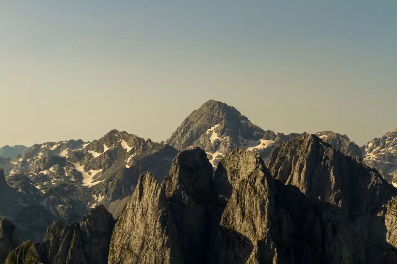 Majestatyczne szczyty Alp Dynarskich, oświetlone słońcem, z resztkami śniegu na zboczach.