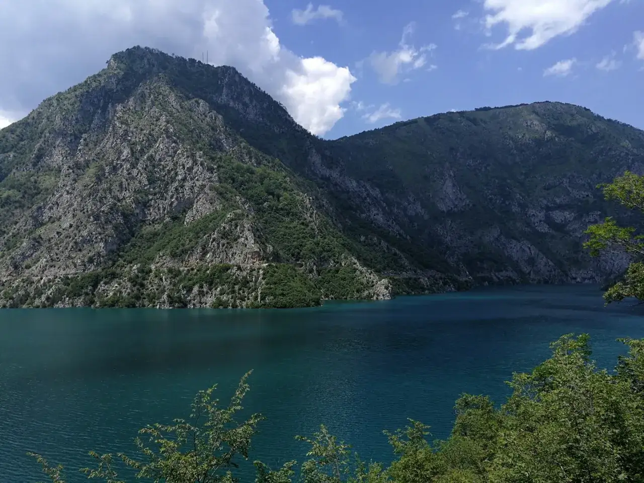 Piękne, turkusowe Pivsko Jezero otoczone skalistymi górami porośniętymi zielenią.