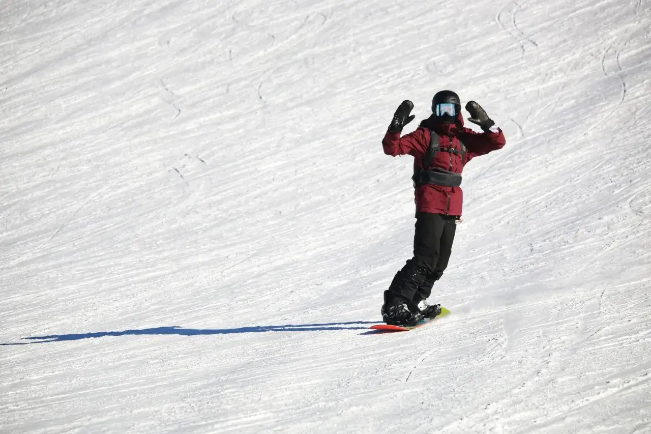 Snowboardzista w czerwonej kurtce z radością zjeżdża po stoku. Zastanawiasz się, ile kosztuje snowboard?