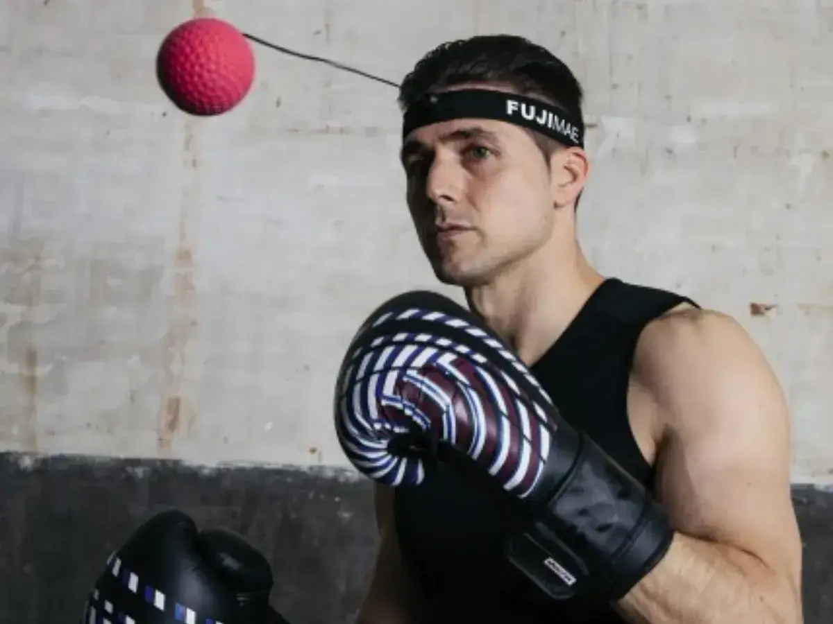 Bokser w rękawicach i opasce FUJIMAE, japoński producent sprzętu sportowego, ćwiczy z piłką refleksyjną.