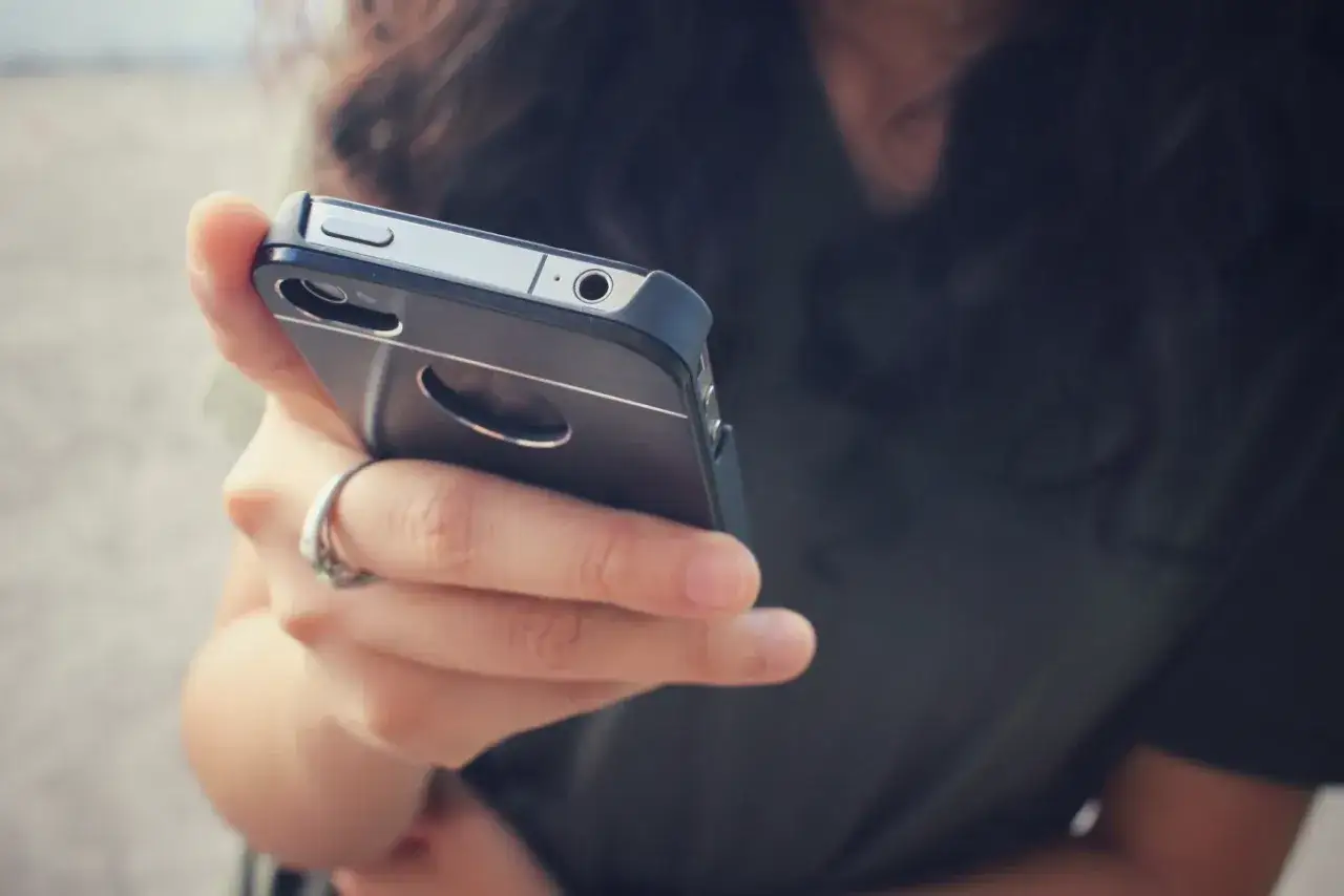 Dłoń z pierścionkiem trzyma telefon. Zastanawiasz się, dlaczego telefon wolno się ładuje? Może to wina kabla lub starej baterii.