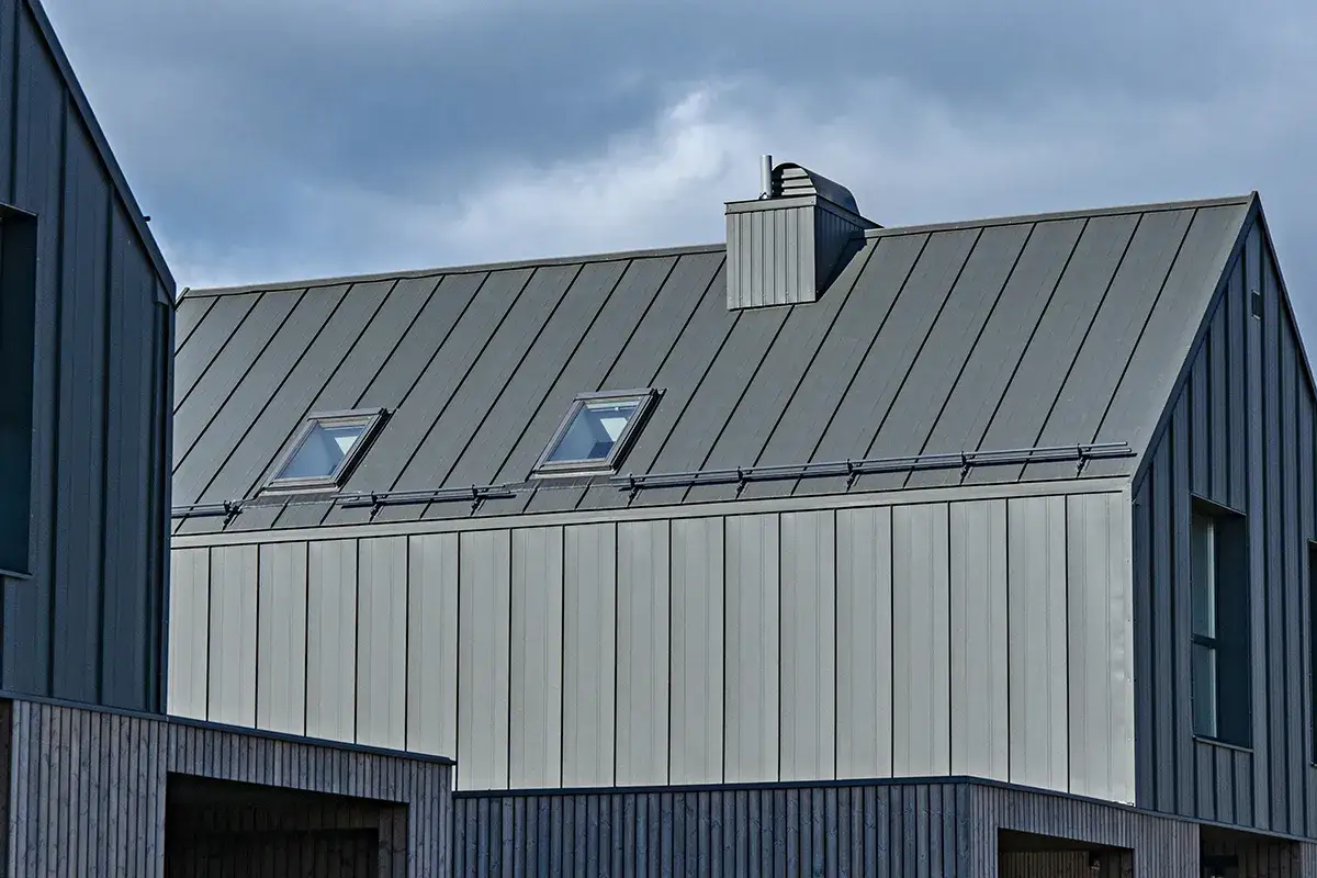 Nowoczesna elewacja z blachy na rąbek, z dwoma oknami dachowymi i kominem.