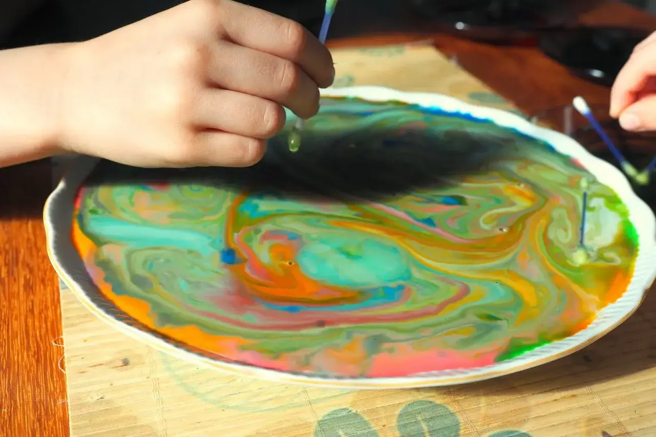 Dziecko dodaje barwniki do mleka, tworząc wirujące, kolorowe wzory.