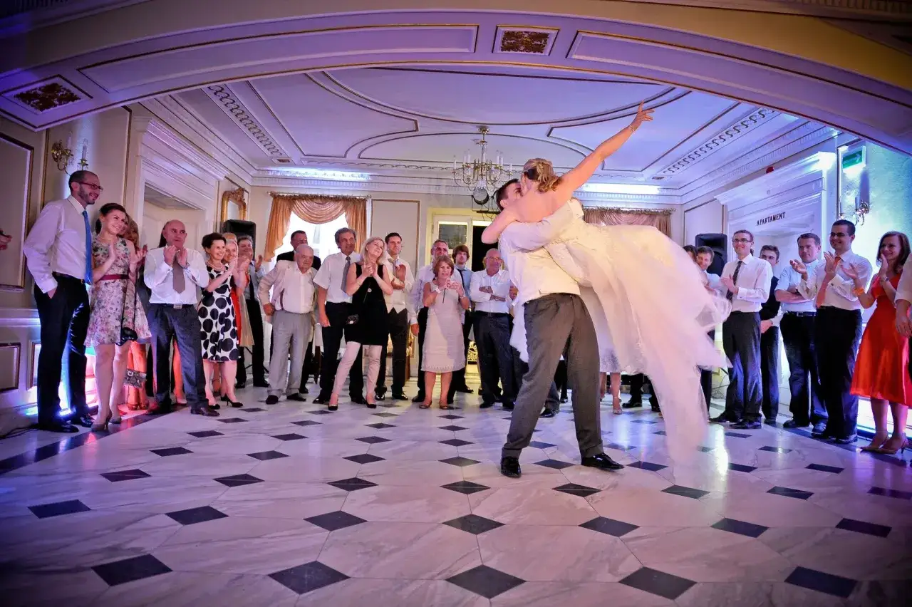 Para młoda tańczy pierwszy taniec na weselu, goście obserwują.