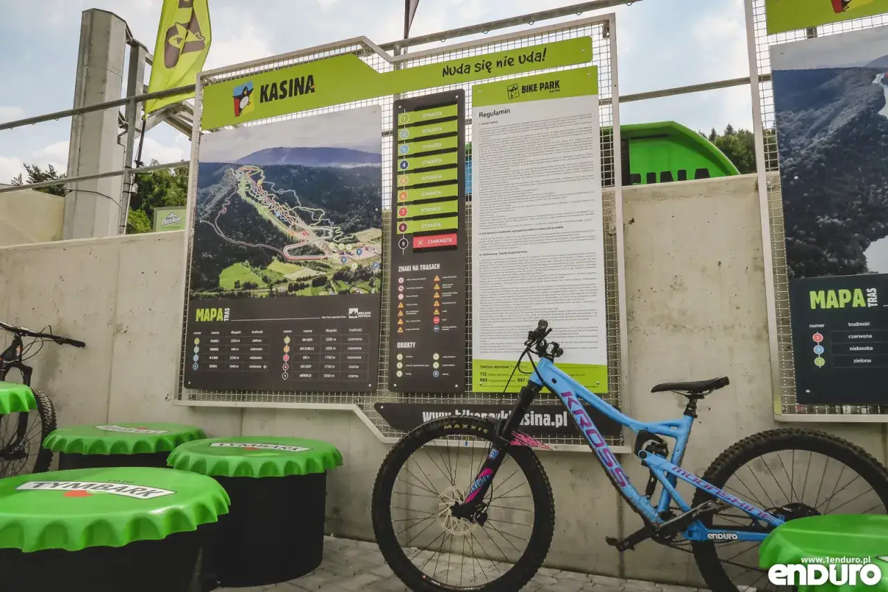 Mapa tras w bike parku Kasina z regulaminem i oznaczeniami trudności. Obok stoi rower enduro.