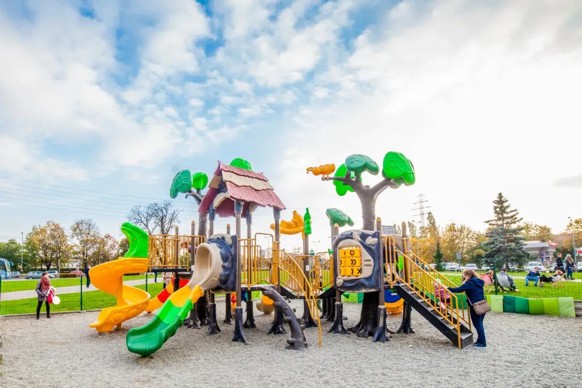 Kolorowy plac zabaw z wieloma zjeżdżalniami i elementami do wspinaczki, pod błękitnym niebem.