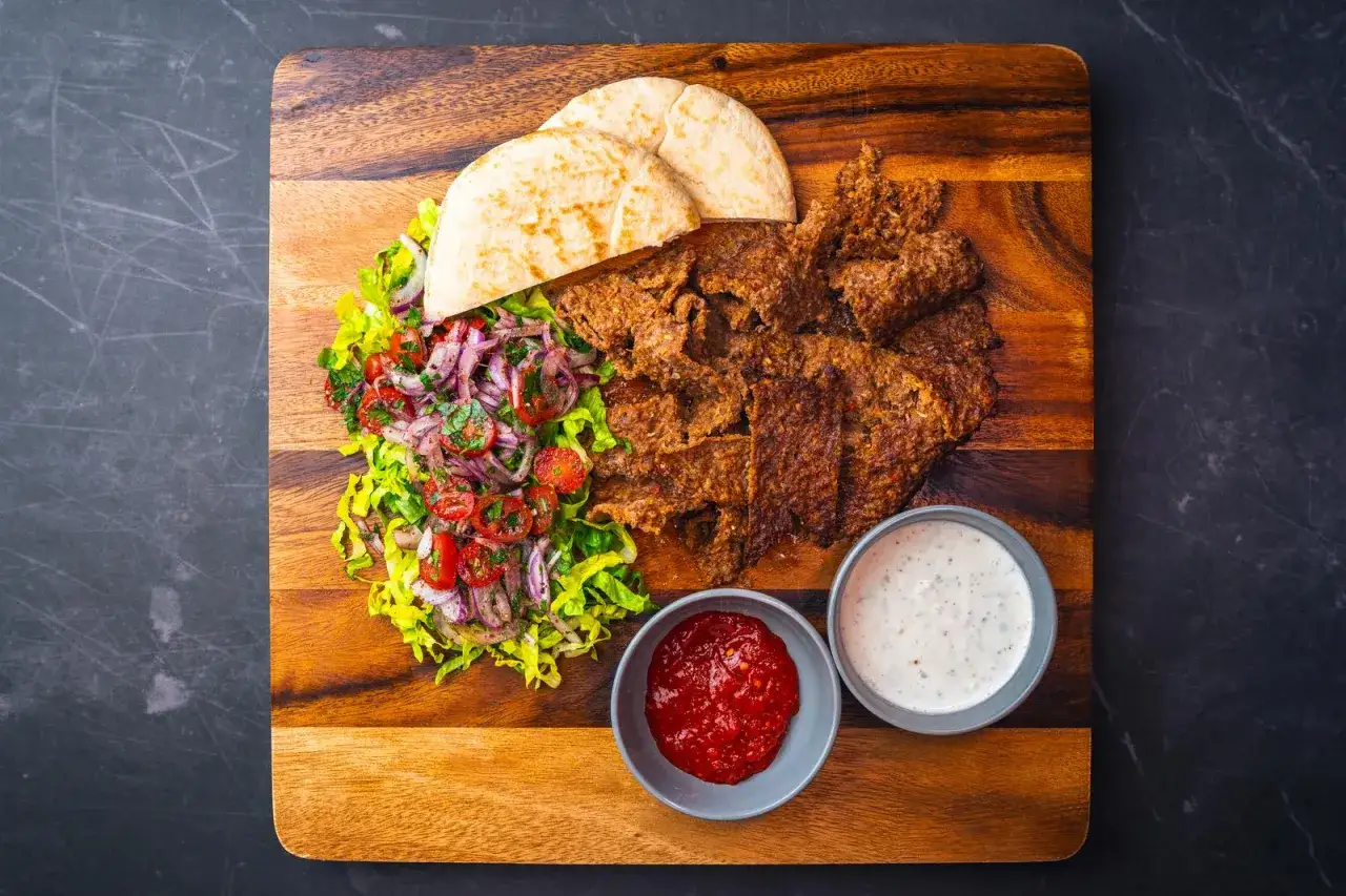Pyszna wolowina do kebaba z sałatką, pitą i sosami na drewnianej desce.