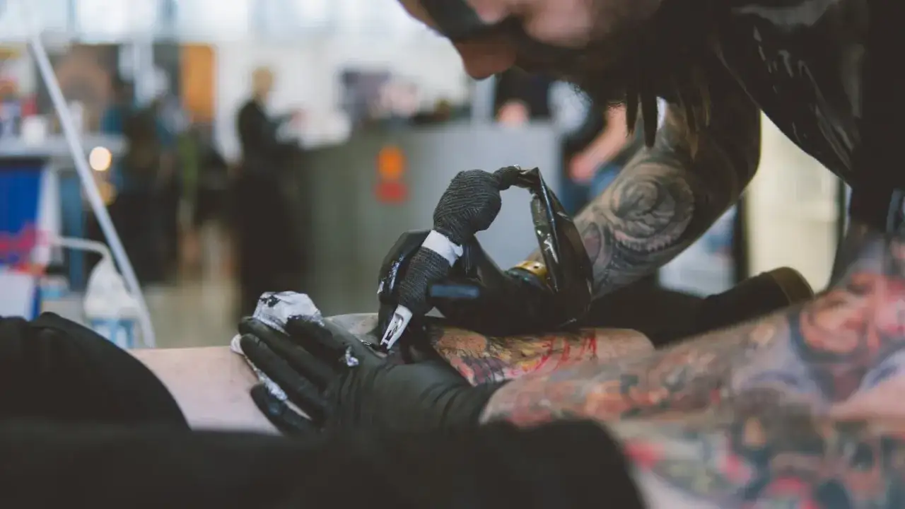 Artysta z tatuażami na ramionach tworzy nowy wzór na nodze klienta. Czy prawnicy mogą mieć tatuaże? Ten obraz pokazuje, że sztuka ciała jest wszędzie.