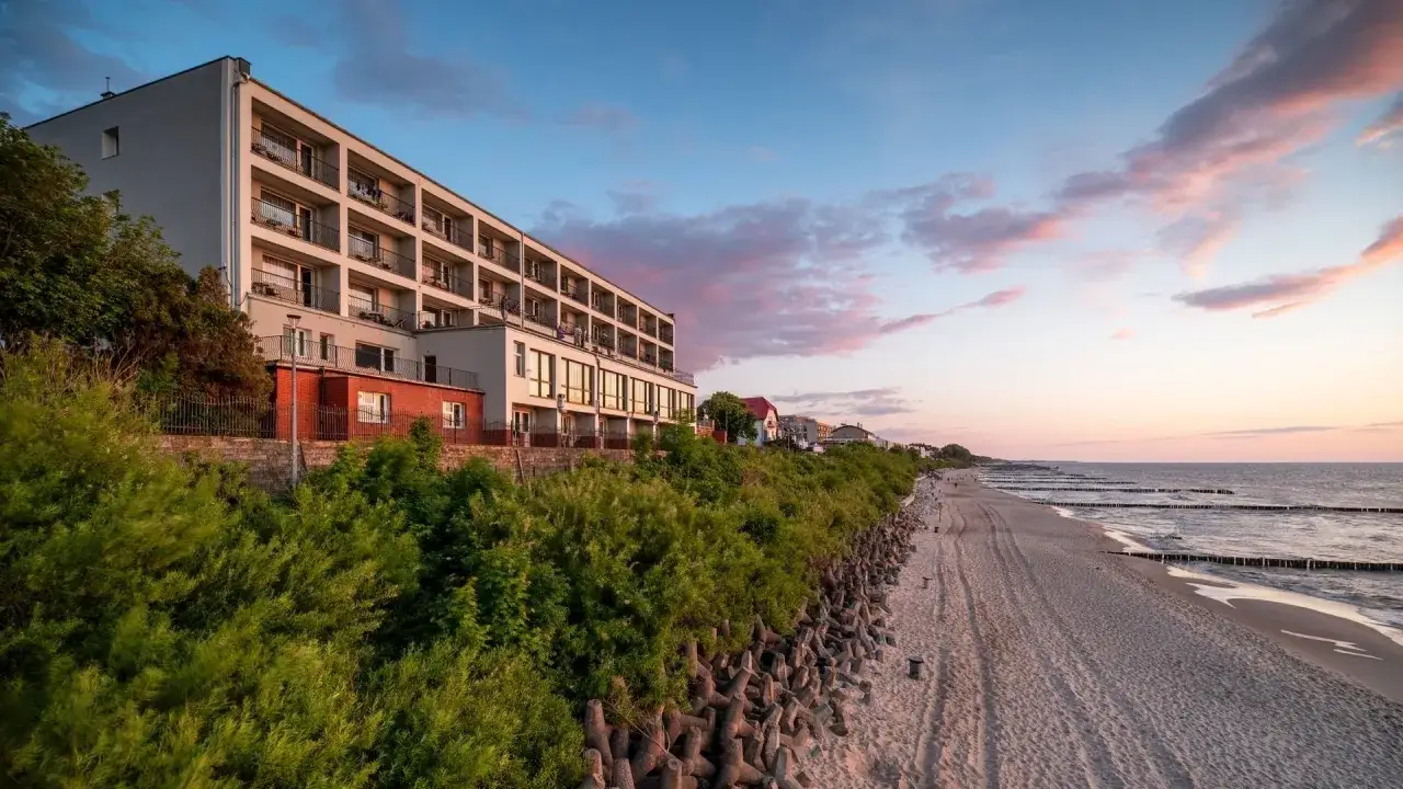 Idealne noclegi przy plaży z widokiem na morze. Hotel z balkonami wychodzącymi na piaszczystą plażę i spokojne morze o zachodzie słońca.