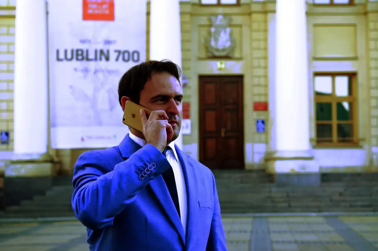 Mężczyzna w garniturze rozmawia przez telefon przed budynkiem z napisem "Lublin 700". Czy adwokat z urzędu jest płatny?