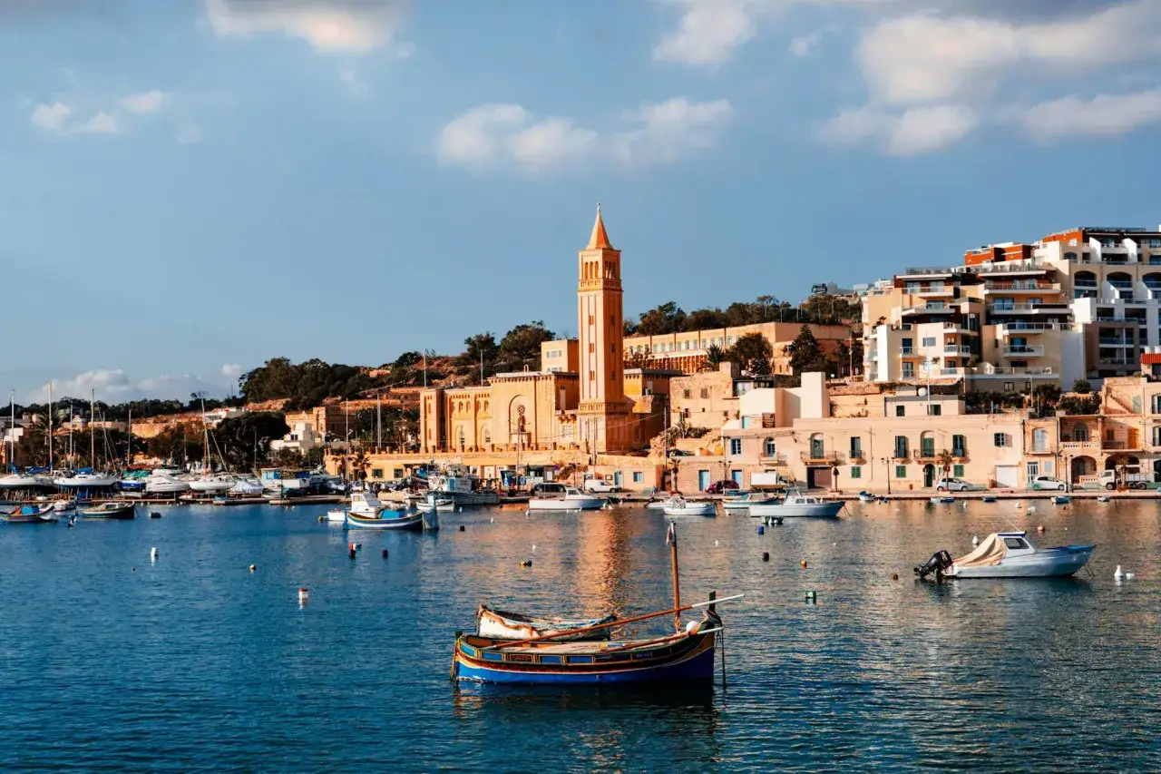 Widok na zatokę z łodziami i budynkami na wzgórzu, w tym wieżą kościelną.