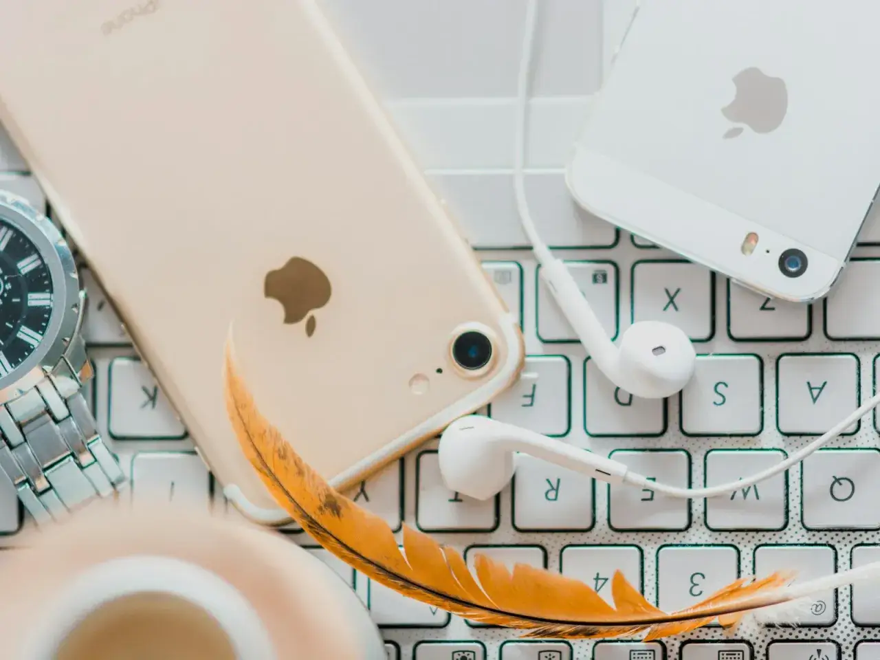 Złoty iPhone, białe słuchawki i piórko na klawiaturze – idealne akcesoria do słuchania audiobooków. Jaka aplikacja do audiobooków sprawdzi się najlepiej?