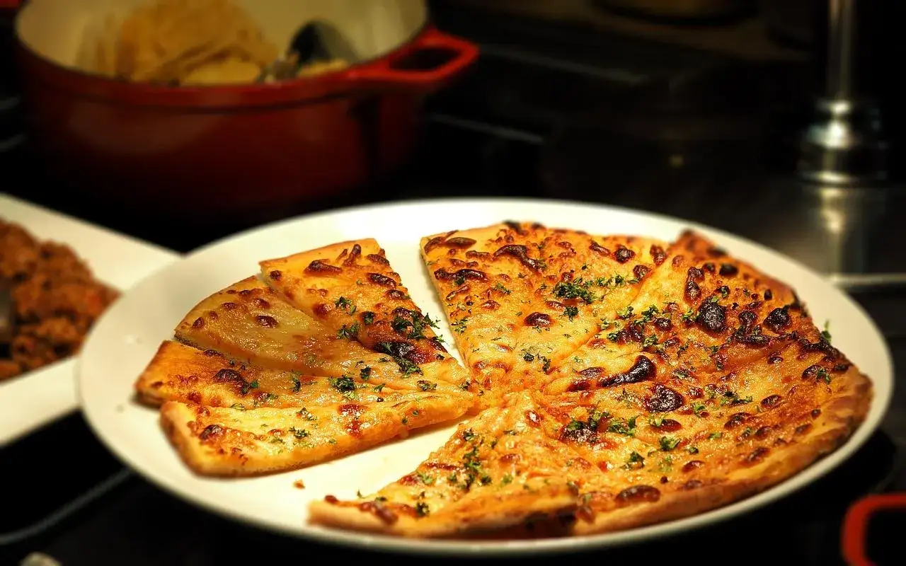 Kawałki pizzy z serem i ziołami na białym talerzu.