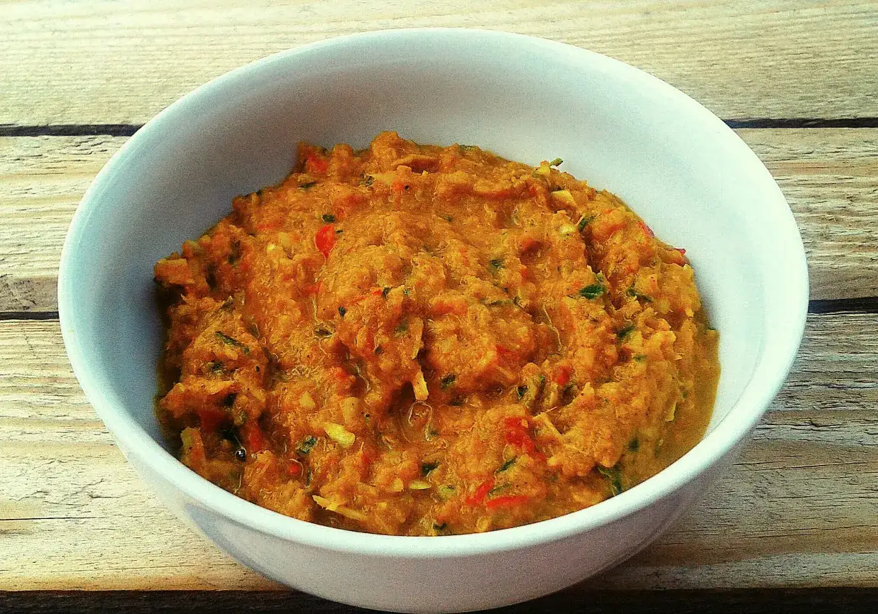 Miska z domową pastą curry o pomarańczowym kolorze, z widocznymi kawałkami warzyw i ziół.
