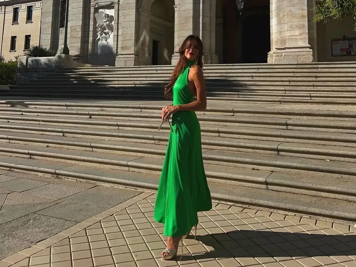 Mujer con vestido verde largo y sandalias plateadas posando en escalinatas de piedra.