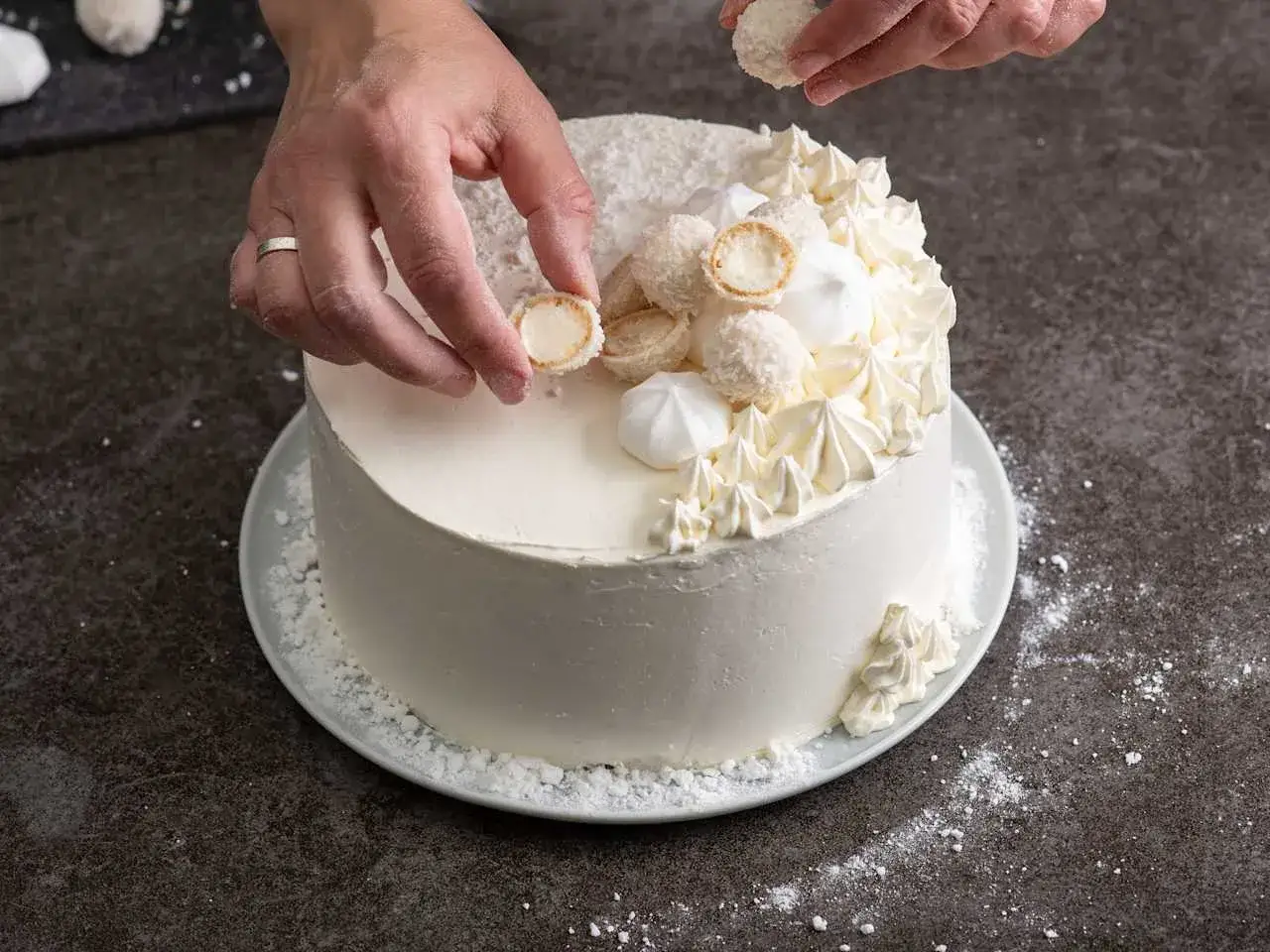 Ozdabianie białego tortu kokosowymi kulkami i bezami.