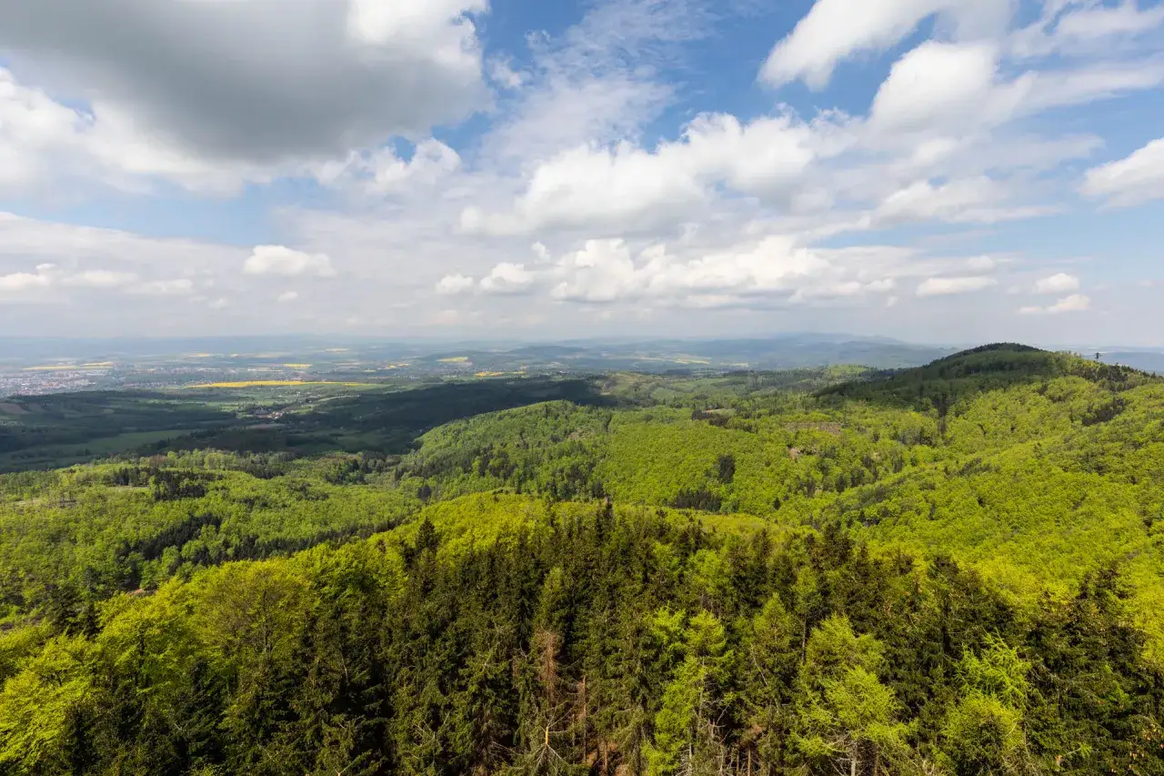 Widok z Kłodzkiej Góry na zielone wzgórza i pola. Chmury na błękitnym niebie.
