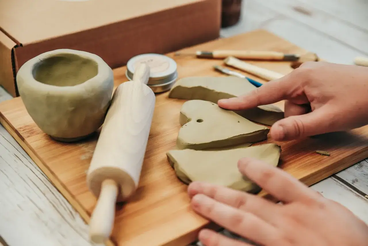 Ręce formują glinę, obok wałek i narzędzia. To idealny zestaw do lepienia z gliny dla początkujących artystów.
