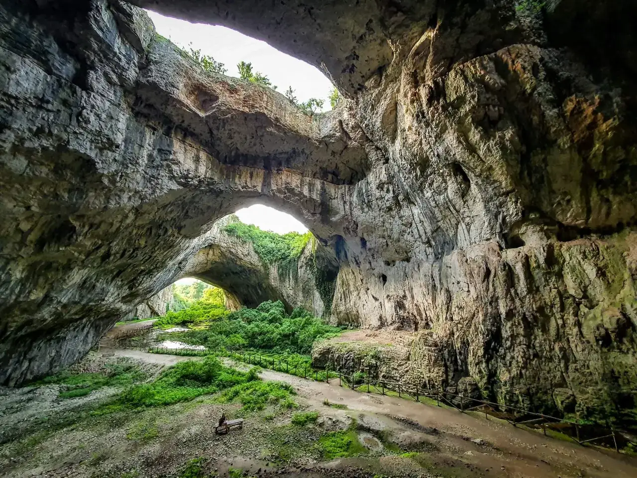 Wielkie skalne mosty w jaskini, przez które widać bujną zieleń. Niezwykłe krajobrazy gór Bałkan.