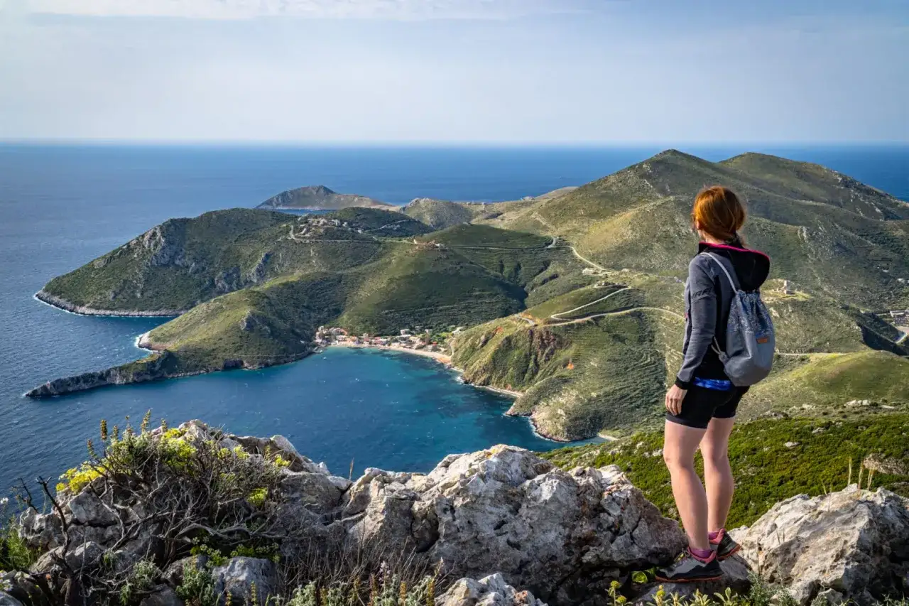 Widok na zatokę i górzysty krajobraz przylądka Matapan. Kobieta z plecakiem podziwia panoramę.