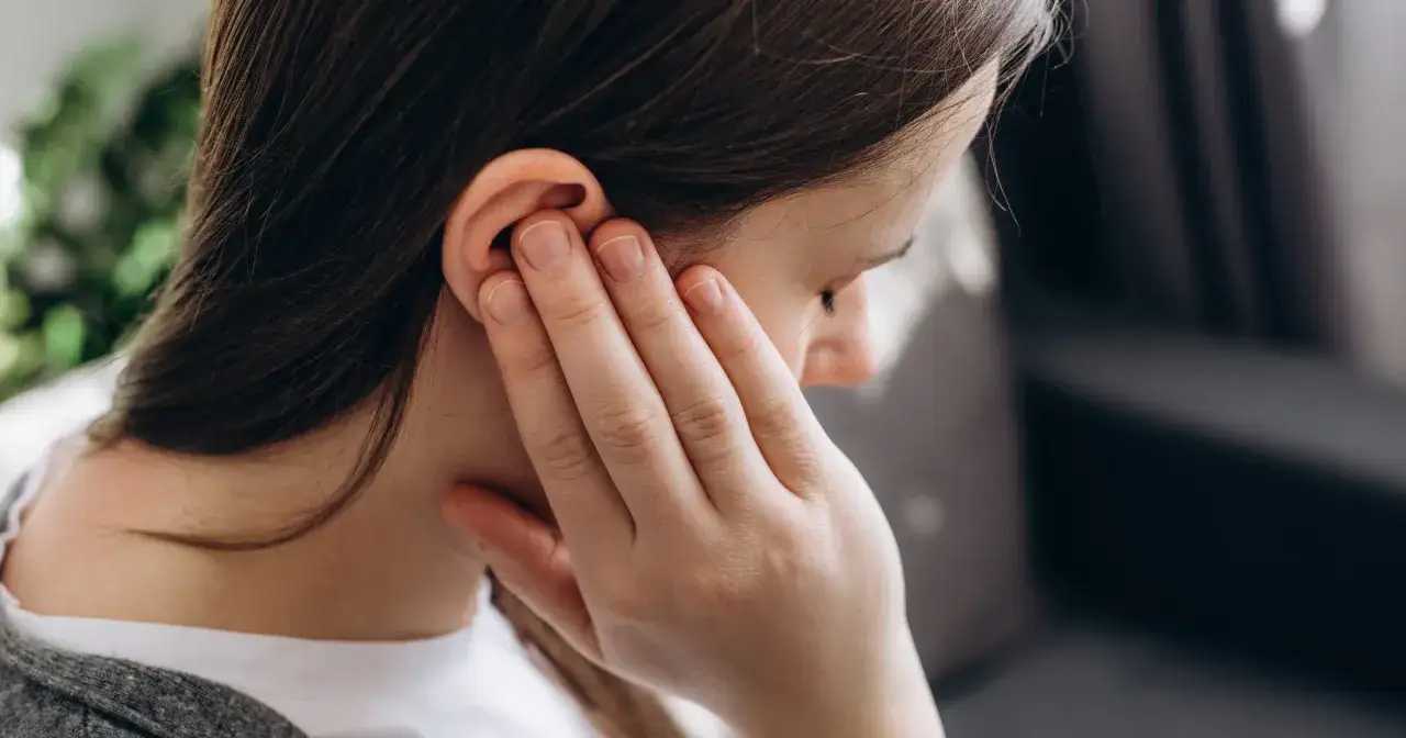 Kobieta z dłonią przy uchu, odczuwająca dyskomfort związany z zatkanym uchem od zatok.