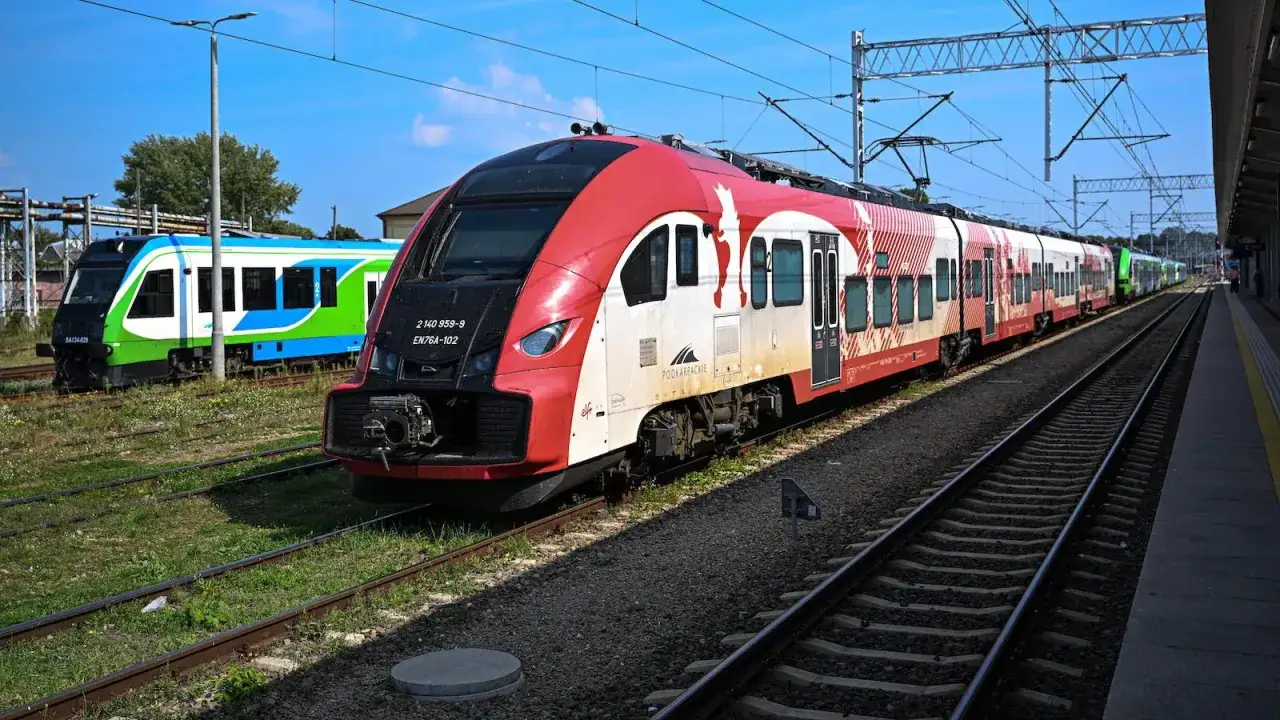 Czerwono-biały pociąg do bukaresztu stoi na torach obok zielono-niebieskiego składu.