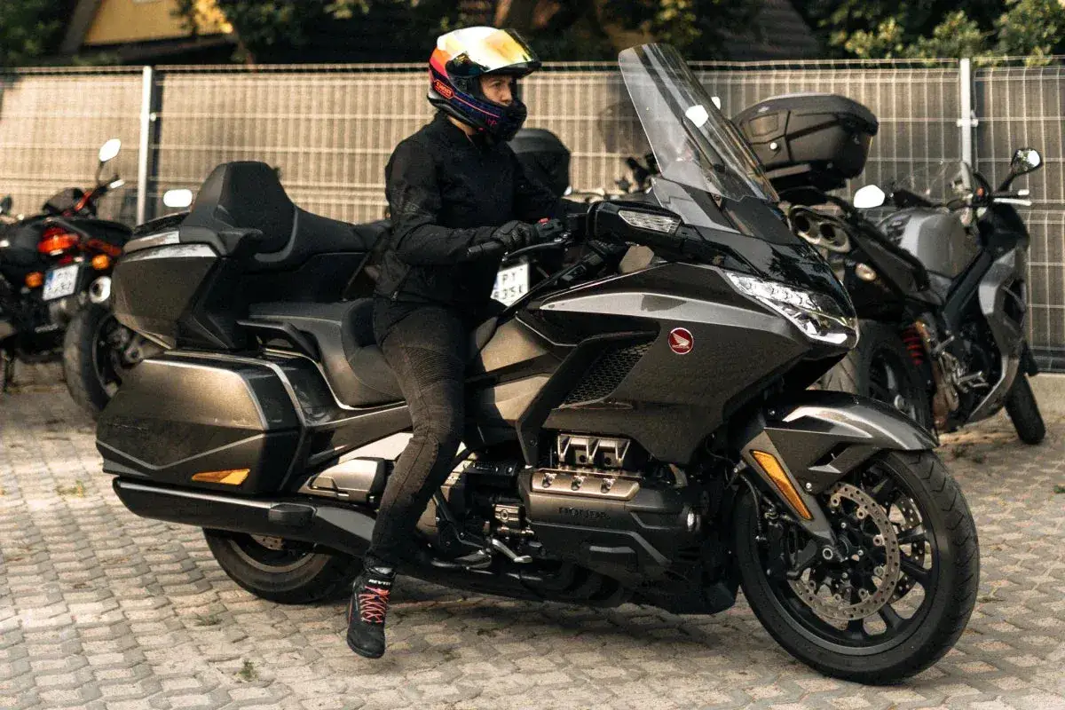 Kobieta w kasku na potężnym motocyklu turystycznym, obok inne rodzaje motocykli.