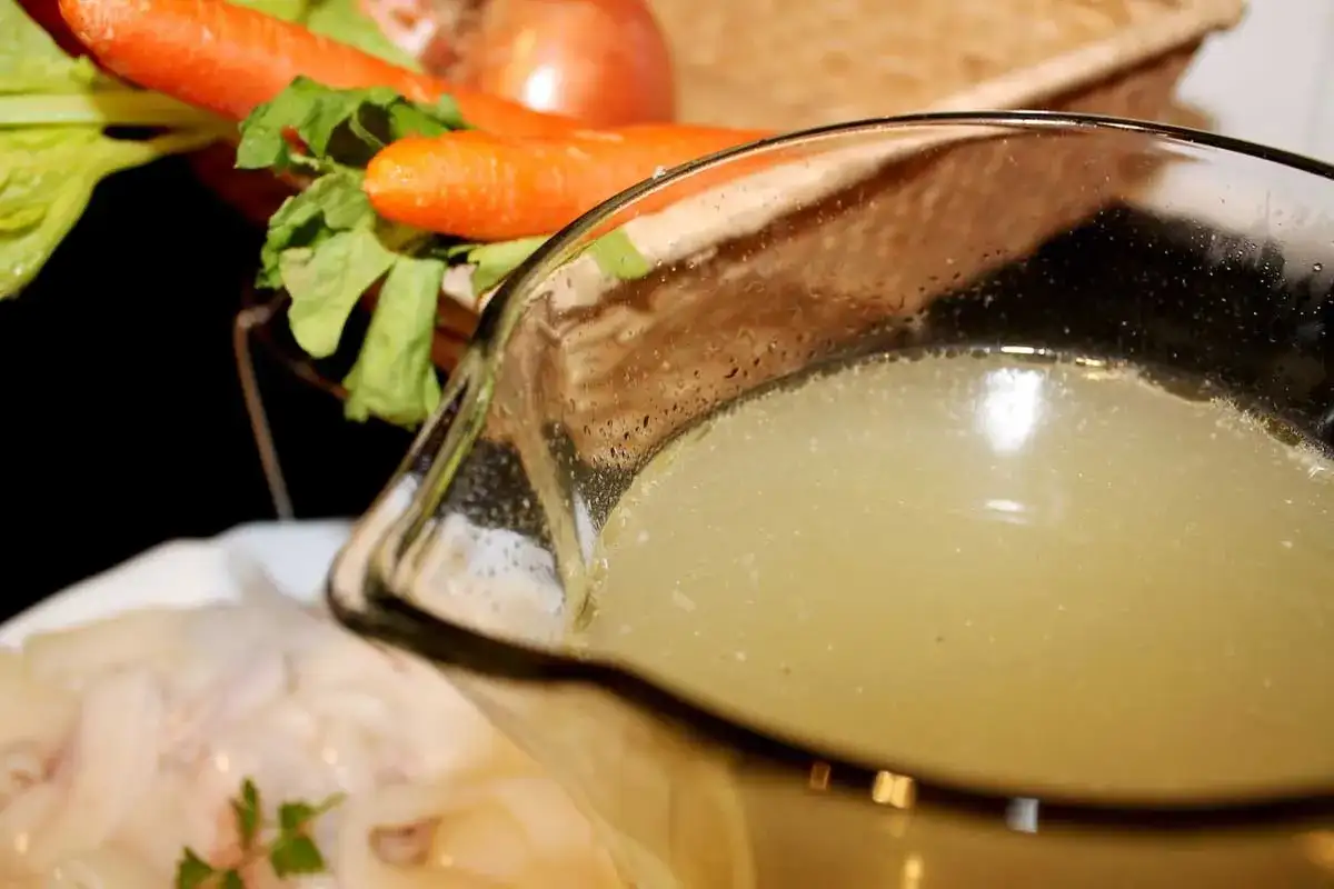 Un delicioso caldo de pescado casero, listo para usar en tu próxima receta. Zanahorias y apio en el fondo.