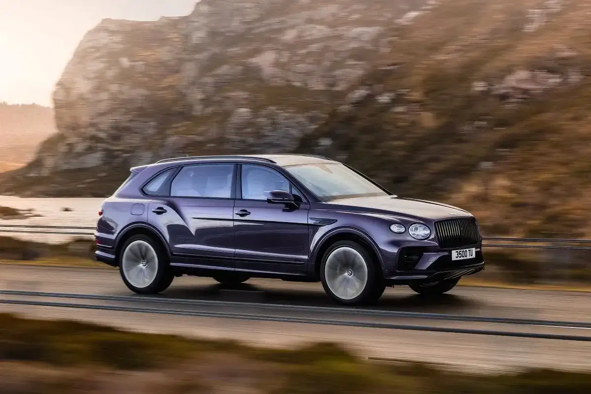 Fioletowy Bentley SUV pędzi po górskiej drodze, otoczony jesiennym krajobrazem.