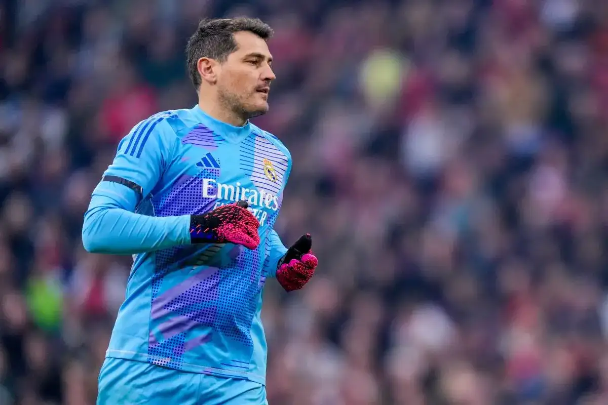 Bramkarz Real Madryt w błękitnym stroju, z różowymi rękawicami, gotowy do obrony. W tle tłum kibiców, symbolizujący drogę do kolejnych trofeów Real Madryt.