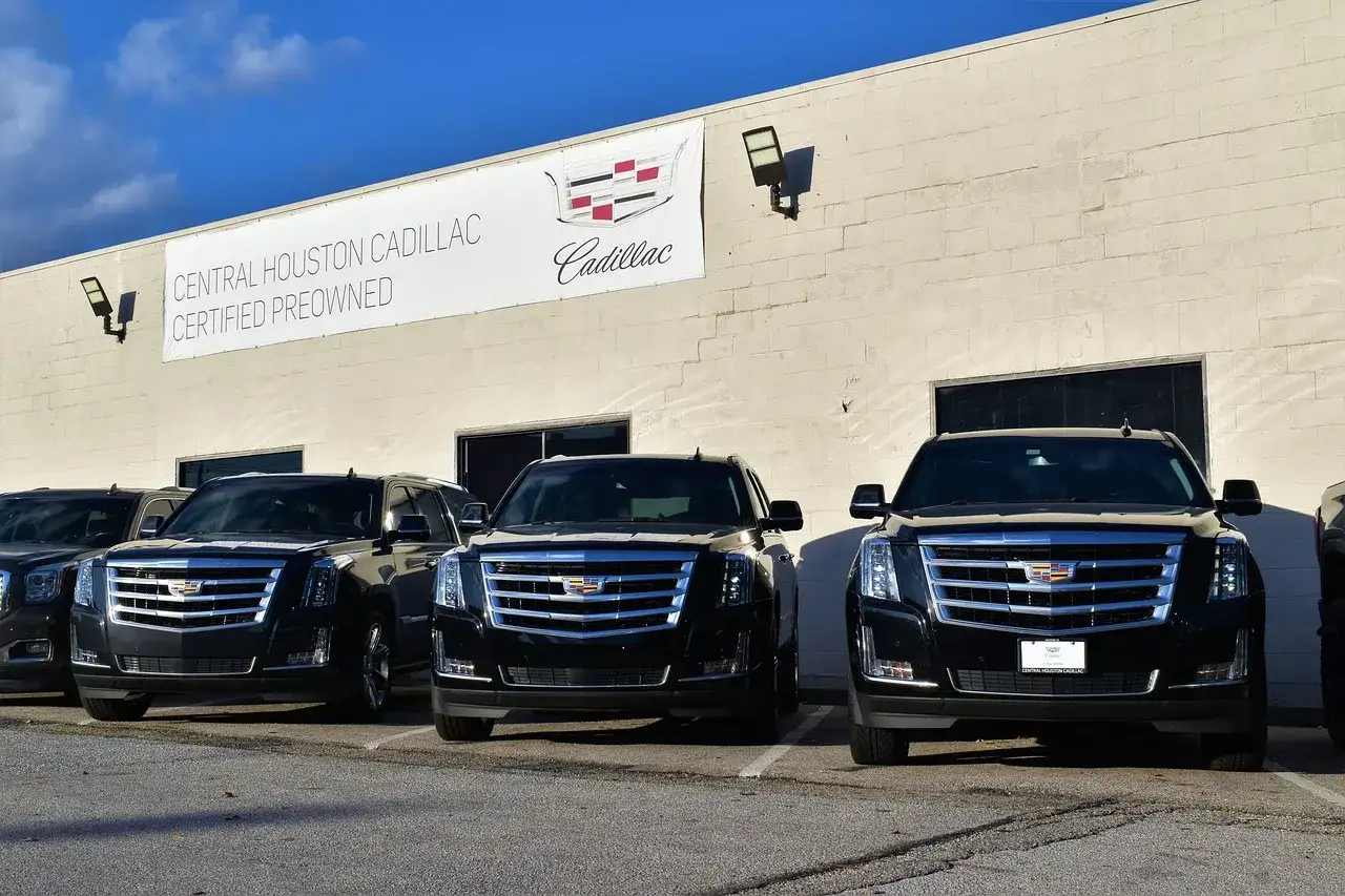 Trzy czarne Cadillac Escalade zaparkowane przed budynkiem salonu samochodowego.