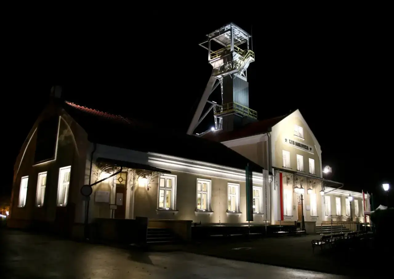 Wieczorem przy szybie kopalni Wieliczka, gdzie można kupić bilety, widać oświetlone budynki i wieżę wyciągową.