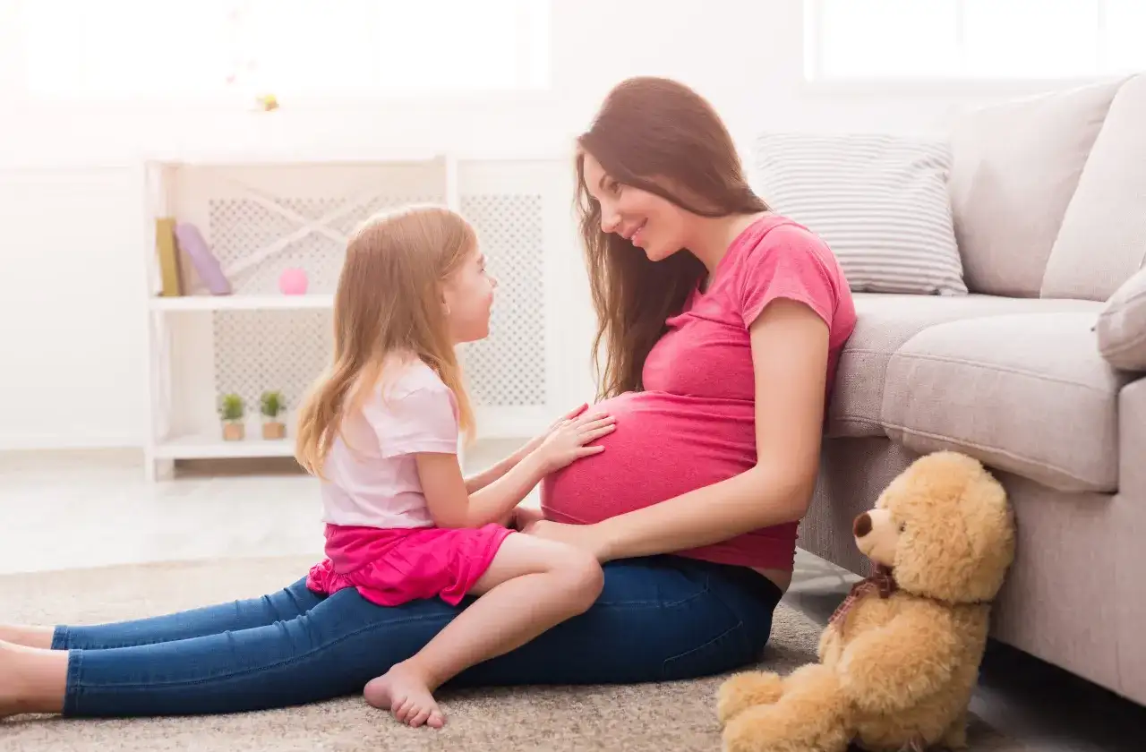 Córka z czułością dotyka brzucha mamy, która wyjaśnia jej, jak wytłumaczyć 10 latkowi skąd się biorą dzieci. Miś czeka na nowego członka rodziny.