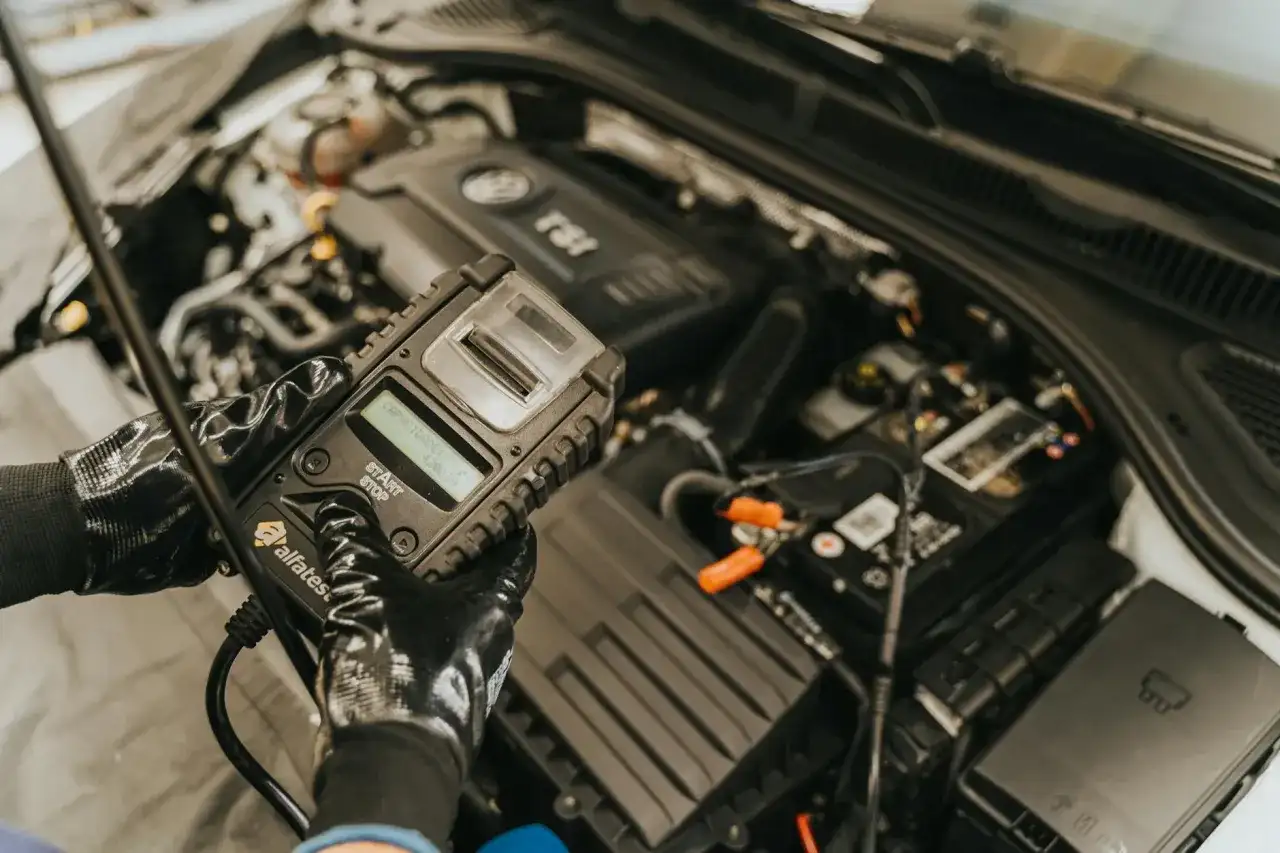 Mechanik w rękawiczkach sprawdza stan akumulatora za pomocą testera, który może również diagnozować czujnik halla w samochodzie.