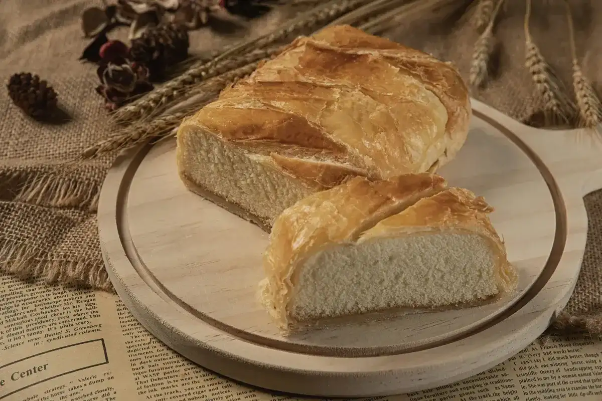Chleb pszenny na desce, z kłosami i szyszkami w tle. Zastanawiasz się, ile kcal ma chleb pszenny?