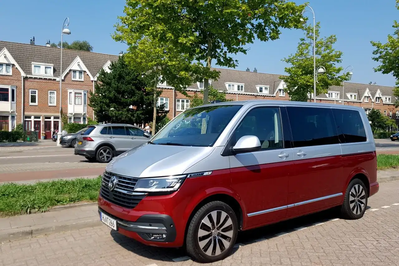 Dwukolorowy volkswagen van, czerwono-srebrny, zaparkowany na tle domów i drzew.