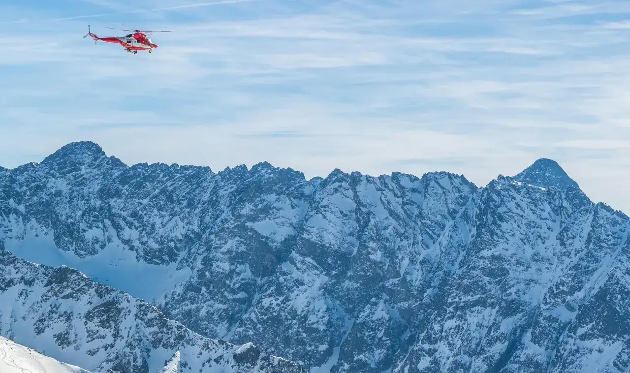 Czerwony helikopter ratunkowy lata nad ośnieżonymi Tatrami.
